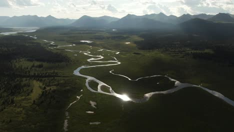 Luftaufnahmen-Eines-Wunderschönen-Grünen-Flusstals-Mit-Bergen-Auf-Beiden-Seiten-Und-Der-Sonne,-Die-Sich-Im-Wasser-Spiegelt