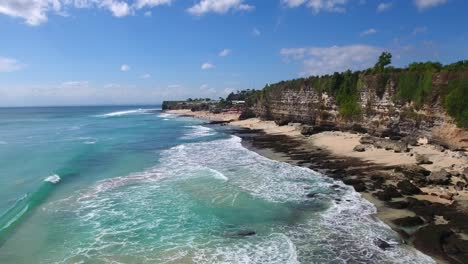 Aerial-view-flying-forwards-of-uluwatu-cliffs-and-beach,-summer-holiday-view-of-tropical-indonesian-beach-with-majestic-rock-cliff,-filmed-in-bali