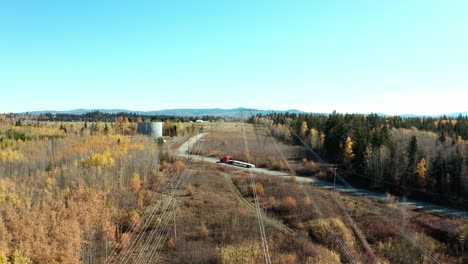 A-cinematic,-moving,-aerial-view-of-some-power-lines-crossing-over-a-back-road-with-an-orange---red-truck-driving-past-during-the-autumn-season