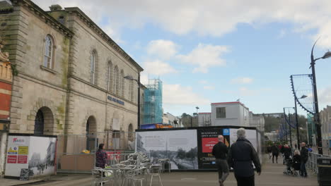 Gente-Caminando,-Leyendo-Los-Detalles-Mostrados-En-Un-Cartel-Fuera-Del-Hall-De-Cornualles,-Truro,-Reino-Unido