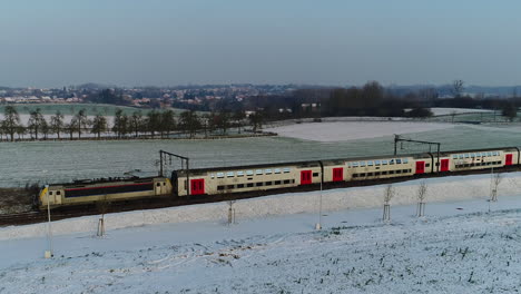 AERIAL:-A-train-riding-through-a-snowy-landscape-on-a-winter-day