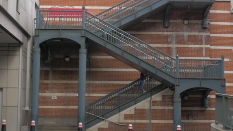 wide,-static-symmetrical-shot-of-man-walking-down-gritty-staircase-in-London