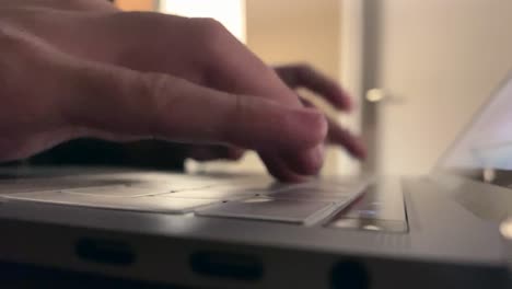 Someone-busy-typing-on-a-keyboard-of-a-aluminium-Apple-MacBook-Pro-laptop-with-touchbar-and-retina-display,-during-the-night-with-a-bright-lamp-on-in-the-background