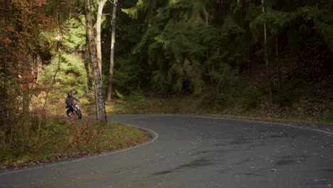 El-Motociclista-Conduce-Por-Una-Carretera-Con-Curvas-A-Través-De-Un-Bosque-Otoñal.