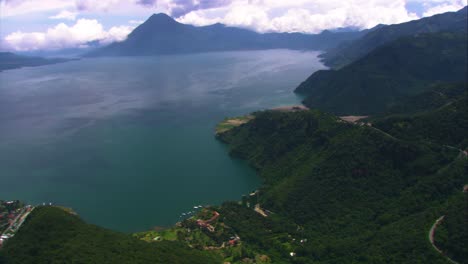 Aerial-view-of-Lake-Atitlan,-showcasing-its-expansive-turquoise-waters,-surrounded-by-lush-greenery-and-towering-volcanoes-under-a-cloudy-sky