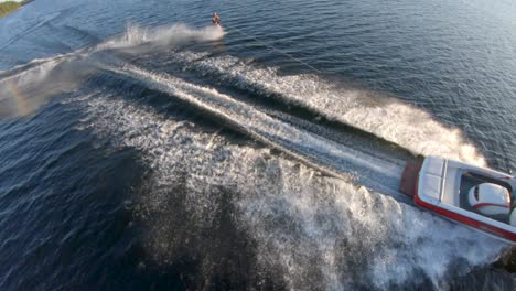 Slow-Motion---White-Man-Slalom-Water-Skis-behind-Boat-on-Blue-Lake-in-Summer-Sunset-Light,-FPV-Drone-Aerial-Tracking