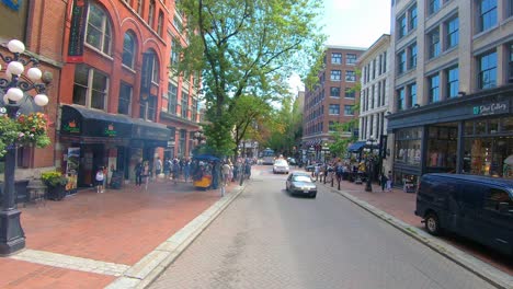 Driving-on-a-small-street-while-people-walking-on-sidewalk-on-sunny-day