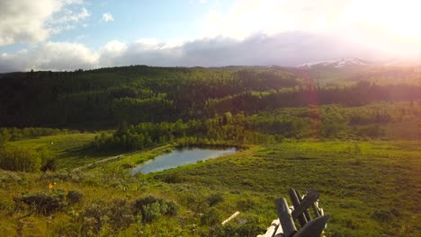 A-panoramic-view-of-a-green-meadow,-mountain-and-pond