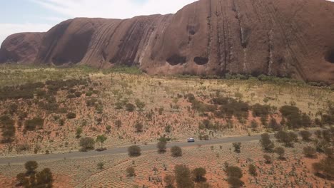 Spektakuläre-Luftaufnahme-Des-Uluru-Ayres-Rock,-Der-Um-Einen-Weißen-Campervan-Kreist