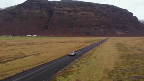 Aerial-view-of-a-Dacia-Duster-SUV-car-driving-on-a-gravel-road-in-the-Icelandic-countryside-with-a-beautiful-mountain-landscape,-Iceland,-Europe,-Orbit-shot