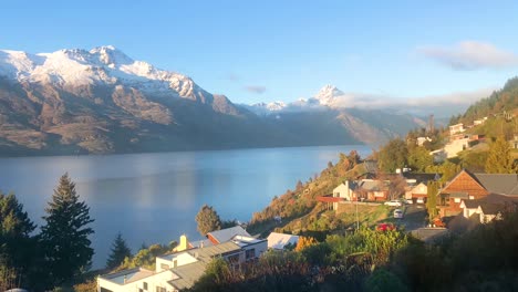 Timelapse-Del-Amanecer-De-Las-Pintorescas-Montañas-Nevadas-De-Nueva-Zelanda-Y-El-Lago-Azul-Con-Los-Residentes-De-Las-Laderas-De-Las-Montañas,-Automóviles-Y-Casas-Bulliciosas-En-Primer-Plano