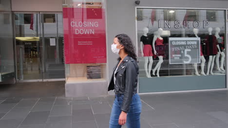 Woman-walking-past-stores-closing-down-with-mask-on-during-coronavirus-pandemic-Bourke-st-Melbourne-Australia