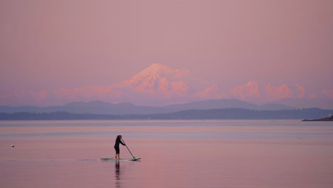 Eine-Person-Beim-Paddleboarding-Bei-Sonnenuntergang-Mit-Schneebedeckten-Bergen-Im-Hintergrund-Auf-Vancouver-Island,-Kanada