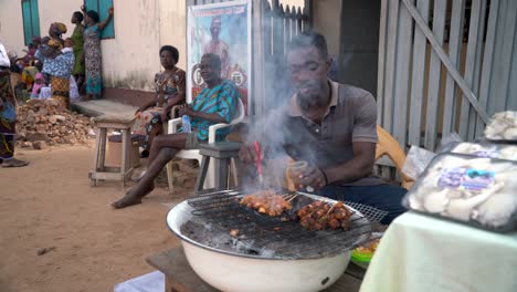 A-man-barbecues-chicken-kabobs-with-vegetables-on-a-grill-outside-his-house,-on-the-street-in-Ghana,-West-Africa