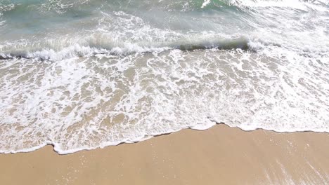 Waves-gently-lap-beach,-calm-summer-scene-with-small-white-water