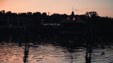 Silhouettes-Of-Two-Women-Paddleboarding-At-The-Lake-Of-Nations-In-Sherbrooke,-Quebec,-Canada-On-A-Sunset---midshot