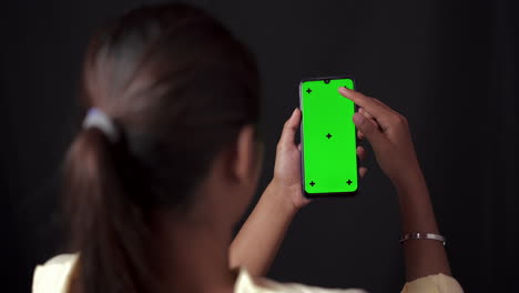 Frau-Hält-Smartphone-Und-Beobachtet-Berührende-Und-Wischende-Inhalte-Auf-Chroma-Key-Greenscreen-Smartphone-In-Schwarzem-Raum