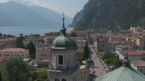 Drone-shot-of-a-church-in-the-center-of-Riva-Del-Garda-with-the-lake-garda-and-the-italian-alps-in-the-background,-Riva-Del-Garda,-small-town-in-Trentino-North-Italy