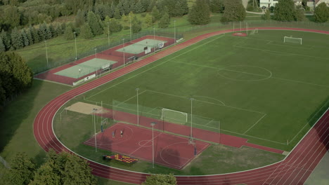 Drone-shot-of-an-empty-football-field-with-teenagers-playing-basketball