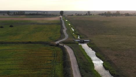 Luftaufnahme-Eines-Motorrads,-Das-Bei-Sonnenuntergang-Eine-Unbefestigte-Landstraße-Entlang-Fährt