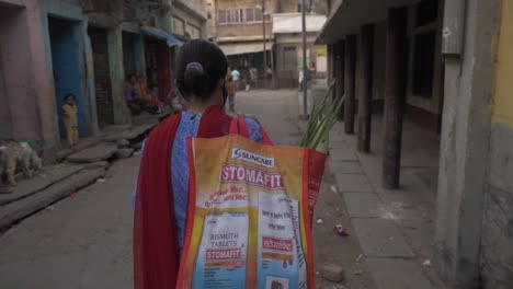 A-girl-wearing-a-mask,-walking-back-with-groceries-in-a-narrow-lane-of-a-village-in-Bihar-state-of-India-during-the-corona-virus-pandemic-lockdown