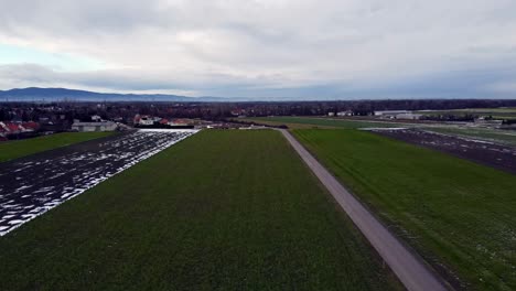 Toma-De-Drones-De-Campos-Marrones-Y-Verdes-En-Invierno-Con-Poca-Nieve-Y-Movimiento-Correcto-Sobre-La-Carretera.