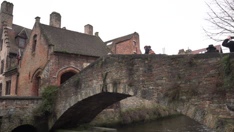 Tilt-down-from-Bonifacius-Bridge-to-the-canal,-while-people-cross-it,-in-Bruges,-Belgium