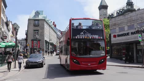 Red-tour-bus-drives-through-busy-streets-of-Montreal,-Quebec-on-a-sunny-day,-Wide-Angle