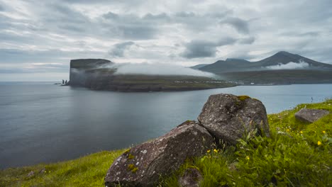 Clouds-passing-green-mountain-cliffs-by-ocean-timelapse-slider-close-up-rocks