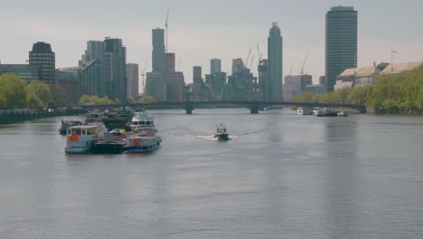 Un-Solo-Barco-Policial-Pasando-Cerca-De-Barcos-Anclados-En-El-Río-Támesis,-Londres,-Vista-Desde-El-Puente-De-Westminster.