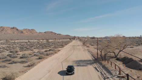 Slow-motion-drone-shot-of-car-going-through-desert-in-Palmdale,-California-on-a-bright-clear-day