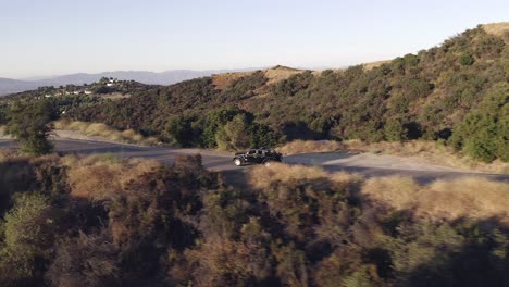 Filmische-Luftaufnahme-Eines-Schwarzen-Jeeps,-Der-Auf-Einer-Asphaltstraße-In-Den-Hügeln-Von-Los-Angeles-Fährt