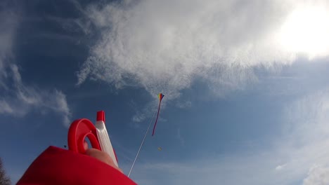 Small-kids-hand,-holding,-and-flying-a-colorful-kite-on-blue-sky,-with-white-clouds-footage