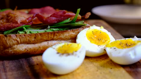 Gesundes-Frühstückssandwich-Auf-Einem-Holzbrett---Hartgekochte-Eier,-Knuspriger-Speck,-Frischer-Spinat-Und-Geröstetes-Weißbrot---Schwenken-Nach-Links