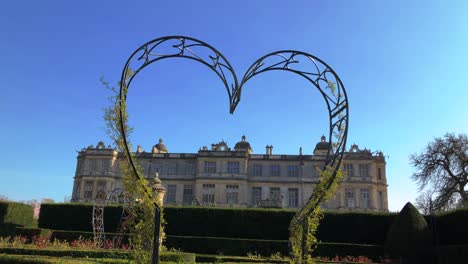 View-Of-Longleat-House-Through-A-Heart-shaped-Garden-Archway-In-Longleat,-Warminster,-UK---low-angle-shot