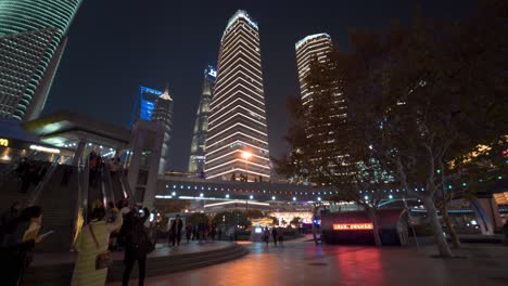 Wide-Angle-Night-life-at-Shanghai-public-square,-slow-reveal-shot-to-skyline