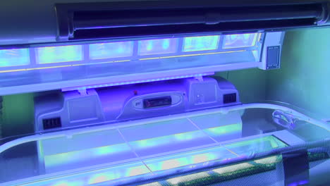 Indoor-tanning-sunbed-pull-back-shot-with-bright-blue-UV-lights-switched-on