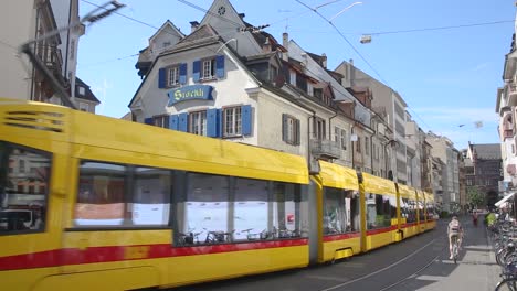 Basel-old-town-busy-street,-modern-yellow-tram-passing-by,-Switzerland