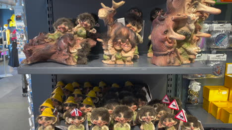 Gifts-of-Troll-souvenir-in-a-Norwegian-shop-for-sale-with-a-tourist-walking-in-the-background,-Pedestal-shot-close-up