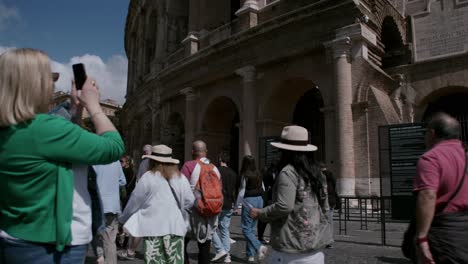 Tourists-stroll-past-weathered-facade-of-the-Roman-Colosseum,-bathed-in-spring-afternoon