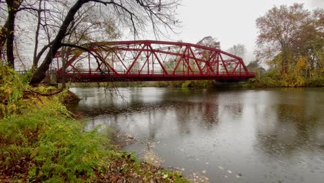 Puente-Rojo,-Arqueado-Y-De-Armadura-Que-Cruza-Un-Río-Durante-El-Otoño-En-Un-Día-Lluvioso