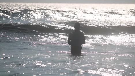 Man-with-a-fishing-net-stands-in-the-sea,-a-wave-crashing-and-splashing-a-man-,-Cox's-bazar-sea-,-Bay-of-Bengal