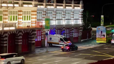 Close-up-shot-of-fire-truck-on-duty-for-emergency-service-exiting-the-main-entrance-of-central-fire-station-at-night-with-traffics-acrossing-on-hill-street,-downtown-Singapore