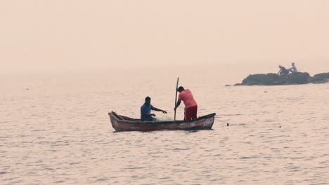 Pescador-Indio-Lanzando-Red-Al-Agua-Durante-La-Puesta-De-Sol-Para-Capturar-Peces-Y-Remando-Un-Pequeño-Bote-De-Madera-En-Medio-Del-Fondo-De-Video-Del-Océano-En-Full-Hd-En-Mov