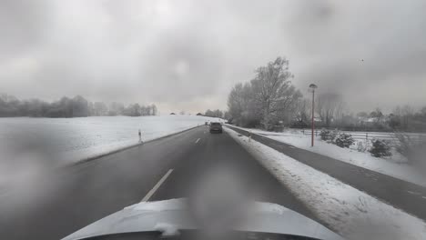 Timelapse-car-drives-through-a-snowy-landscape-from-drivers-front-view-in-the-winter-season-with-real-snowflakes-on-the-camera-lense---cam-on-the-car-roof