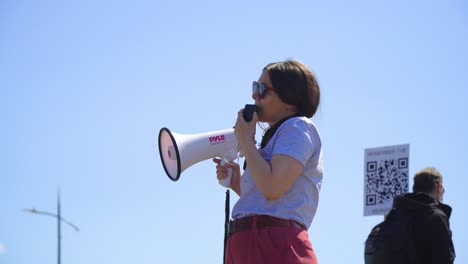 Liderar-A-Una-Protestante-Hipster-Femenina-Dando-Instrucciones-Y-Brindando-Información-A-Los-Participantes-Del-Evento-En-Un-Día-Brillante-Y-Con-Un-Cielo-Despejado.