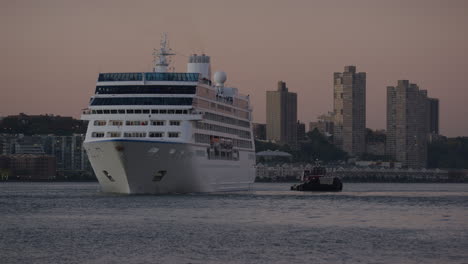 Forward-Bow-Of-Passenger-Cruise-Ship-Being-Assisted-By-Tug-Boat-On-River-Hudson-During-Sunset-With-New-Jersey-In-Background