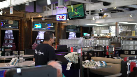 Mels-Drive-in-Diner-Bar,-Pub,-Diner,-Restaurant-In-Hollywood,-Los-Angeles,-Kalifornien,-USA,-Mit-Jukebox-Zum-Abspielen-Von-Alten-Songs-Und-Leuchtendem-Neon-Barschild-Im-Hintergrund,-Im-Fernsehen-Läuft-Ein-Sportspiel