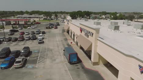 An-aerial-drone-view-of-an-electric-Amazon-delivery-van-making-deliveries-in-a-shopping-center-in-Clear-Lake,-Houston,-Texas