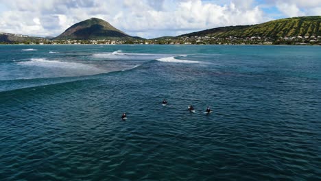 Close-up-aerial-footage-of-four-male-asian-hawaiian-surfers-in-wetsuits-sitting-on-their-surfboards-as-they-wait-for-waves